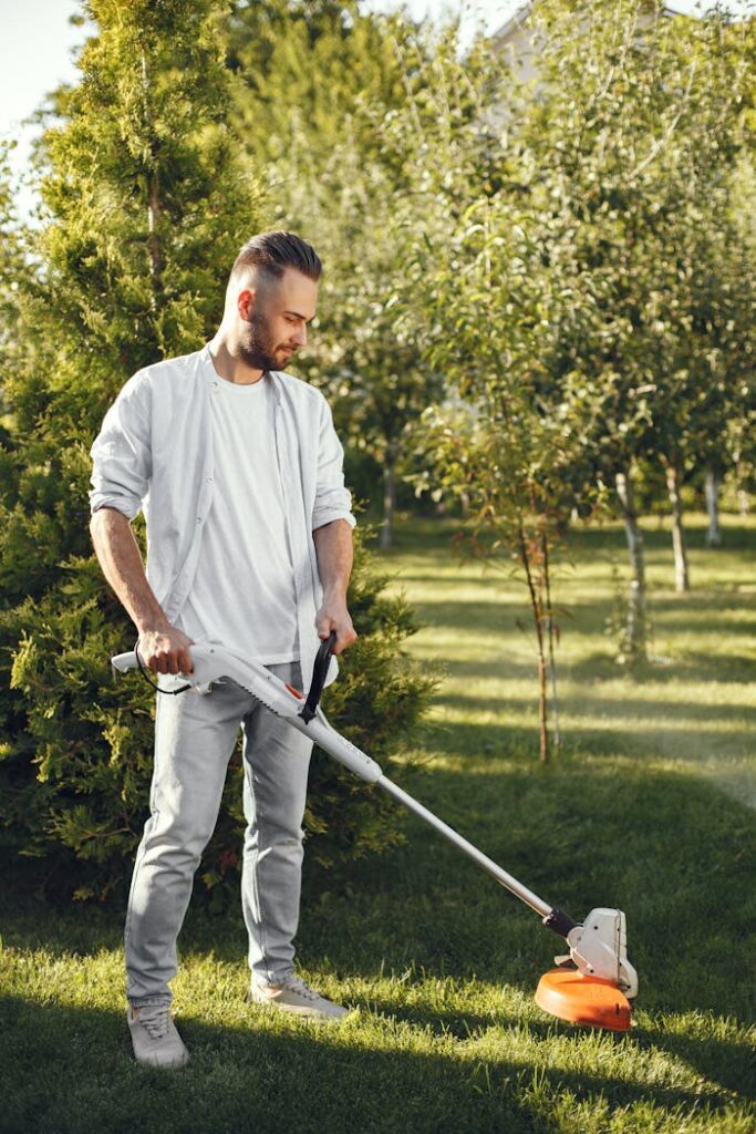 pexels-photo-5163442 Man using a grass cutter to trim the lawn in a sunny garden. Outdoor gardening activity.